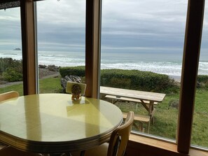 A table and chairs inside a room with a large window overlooking the ocean. - Dot's Beachfront Bungalow Off-Grid Haven (Arch Cape)