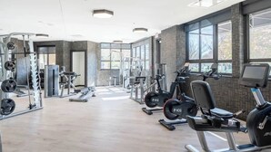 Una palestra con macchinari cardio, attrezzature per sollevamento pesi e ampie finestre.