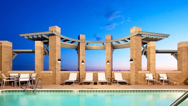Area piscina con struttura a pergola, sedie a sdraio e vista libera sul cielo.