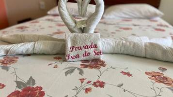 Una cama con ropa de cama floral y una toalla con forma de corazón que tiene una etiqueta que dice 'Porrada da Sol'.