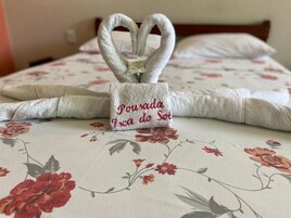 Una cama con ropa de cama floral y una toalla con forma de corazón que tiene una etiqueta que dice 'Porrada da Sol'.