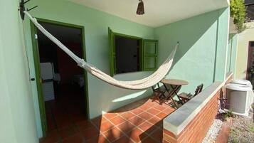 Una hamaca en un balcón con suelo de baldosas, una mesita y una silla.