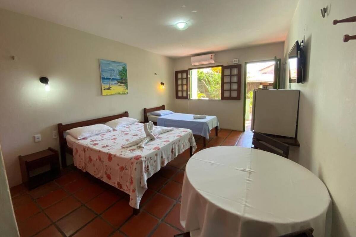 A room with two beds, a round table, a painting, and an air conditioning unit.