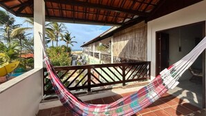 Un hamac sur un balcon avec vue sur des palmiers et un immeuble.