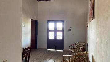 Una habitación con piso de baldosas, una puerta con dos ventanas y dos sillas de mimbre.