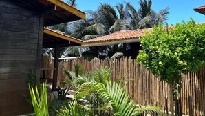Un cadre tropical avec une maison en bois, une clôture en bambou et une végétation luxuriante.