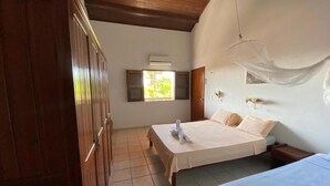 Une pièce comprenant un lit, une armoire en bois, une fenêtre avec des volets et un luminaire suspendu.