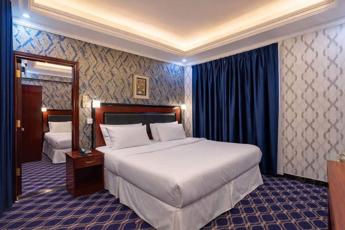 A hotel room with a large bed, a nightstand, a mirror, and a patterned carpet.