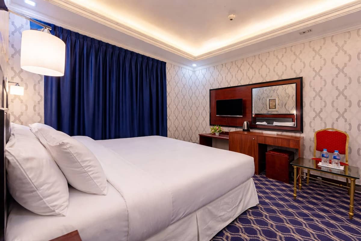 A hotel room with a large bed, a desk, a mirror, and a television.