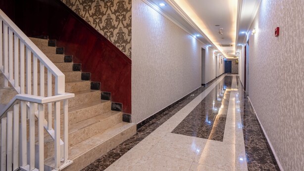 A hallway with a marble floor, a staircase with a red accent, and patterned wallpaper. - Gulf Star Hotel (Dubai)