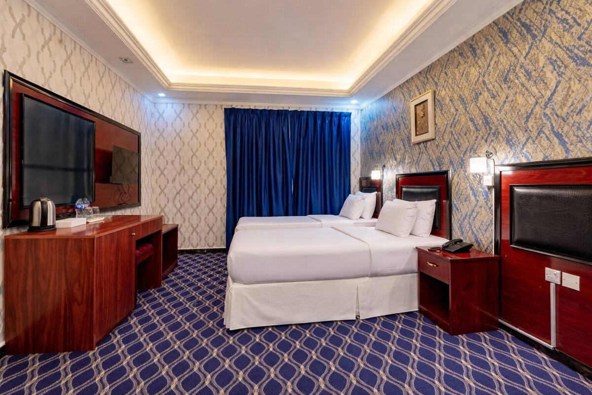 A hotel room with a large bed, a desk with a flat-screen TV, a minibar, and a patterned carpet.