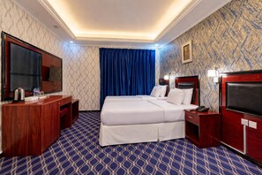 Habitación de hotel con una cama grande, un escritorio con televisor de pantalla plana, un minibar y una alfombra estampada.
