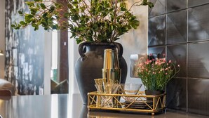 A modern kitchen with a marble countertop, a large vase with green foliage, and a gold tray with glassware.