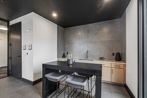 Een moderne keuken met een donker aanrecht, twee barkrukken, een spoelbak en een vaas.