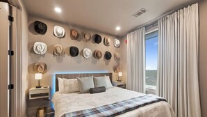 A bedroom with a bed, bedside tables, a headboard, and a wall of hats.
