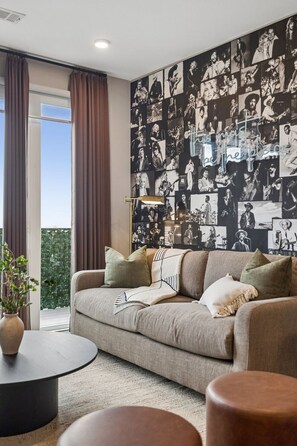 Een moderne woonkamer met een groot muurschildering, een bank, een bijzettafeltje en uitzicht op groen.