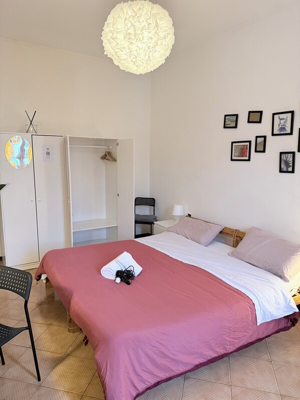 A hotel room with a bed, a wardrobe, a desk, a chair, and a wall with framed pictures.