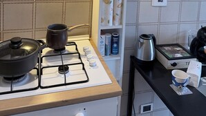 A kitchen with a gas stove, a pot on it, a coffee maker, and a shelf with various items. - Vanilla Center-2 Rooms DBL+ Equipped Kitchen (Torino)
