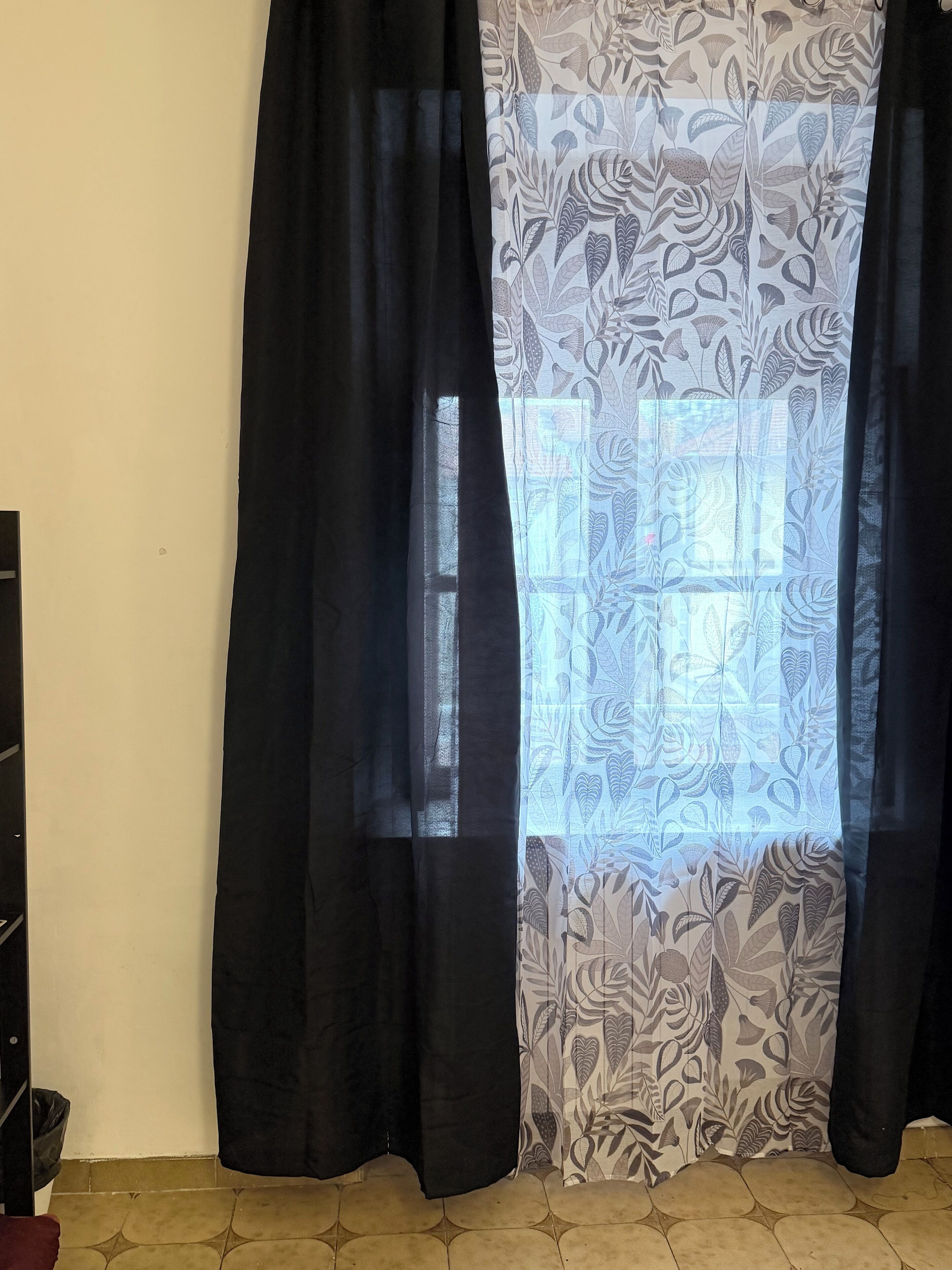 Una habitación con ventana, cortinas negras y cortinas estampadas.