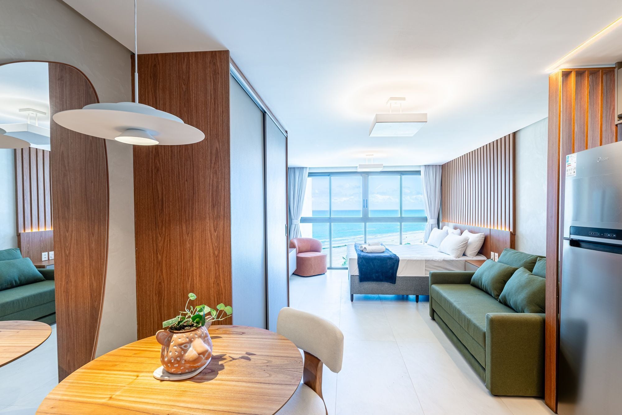 A modern interior with a dining area, a sofa, a bed, and a view of the ocean.