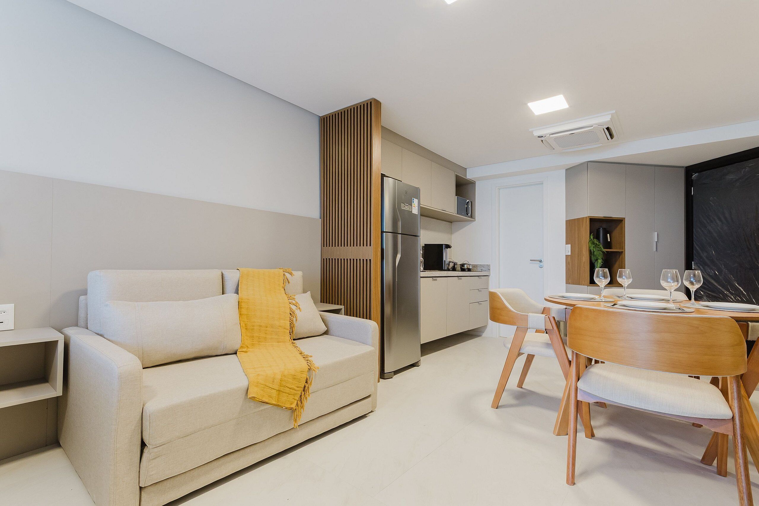 Una sala de estar moderna con un sofá, una mesa de comedor con sillas, una zona de cocina y una pantalla negra en la pared.