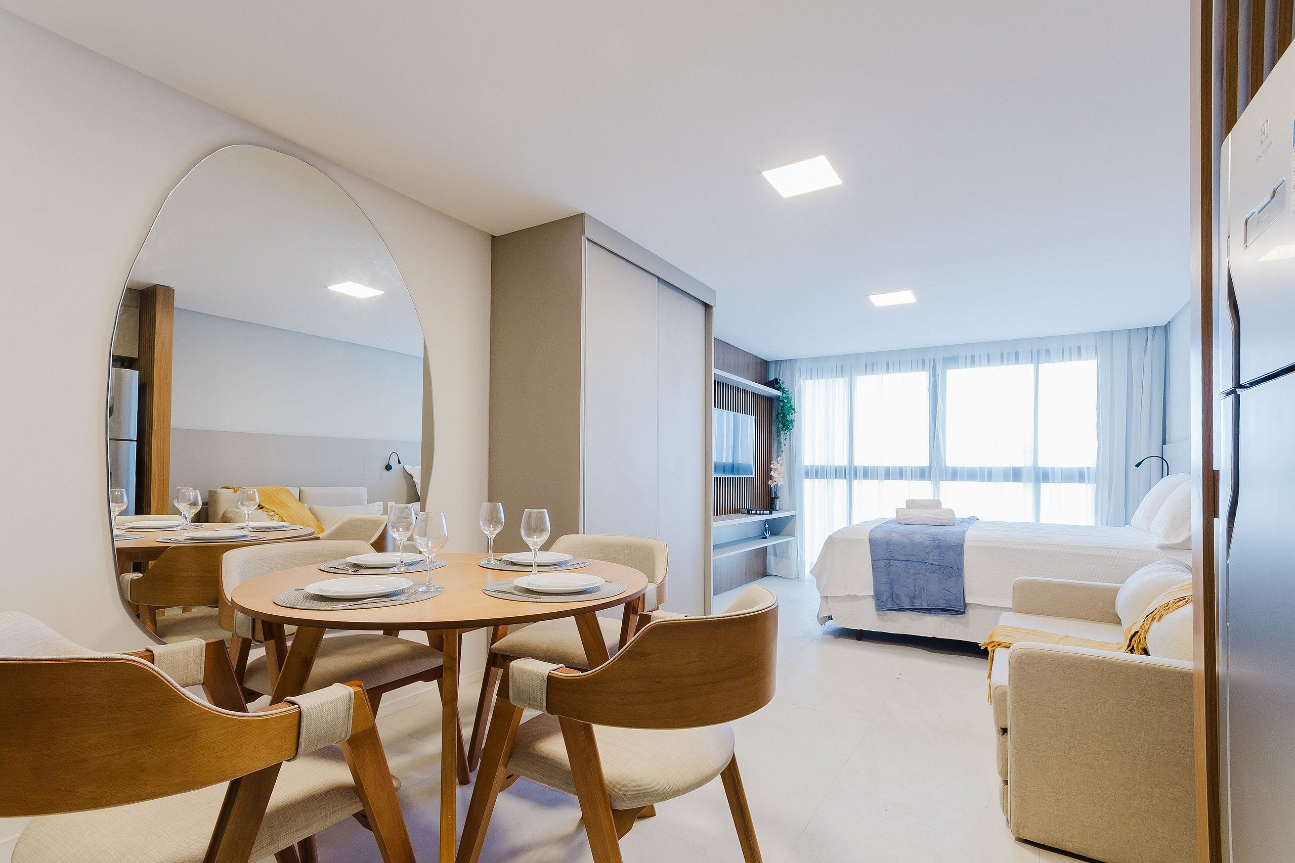 A modern hotel room with a dining area, a bed, and a large window.