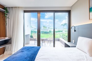 A modern bedroom with a large bed, a view of a garden through a sliding door, and a small seating area with a table and chairs. - Vivant New Building Seafront in Recife (Recife)