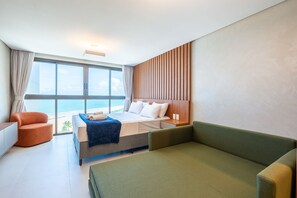 A hotel room with a bed, a green sofa, a small orange chair, and a view of the ocean. - Vivant New Building Seafront in Recife (Recife)