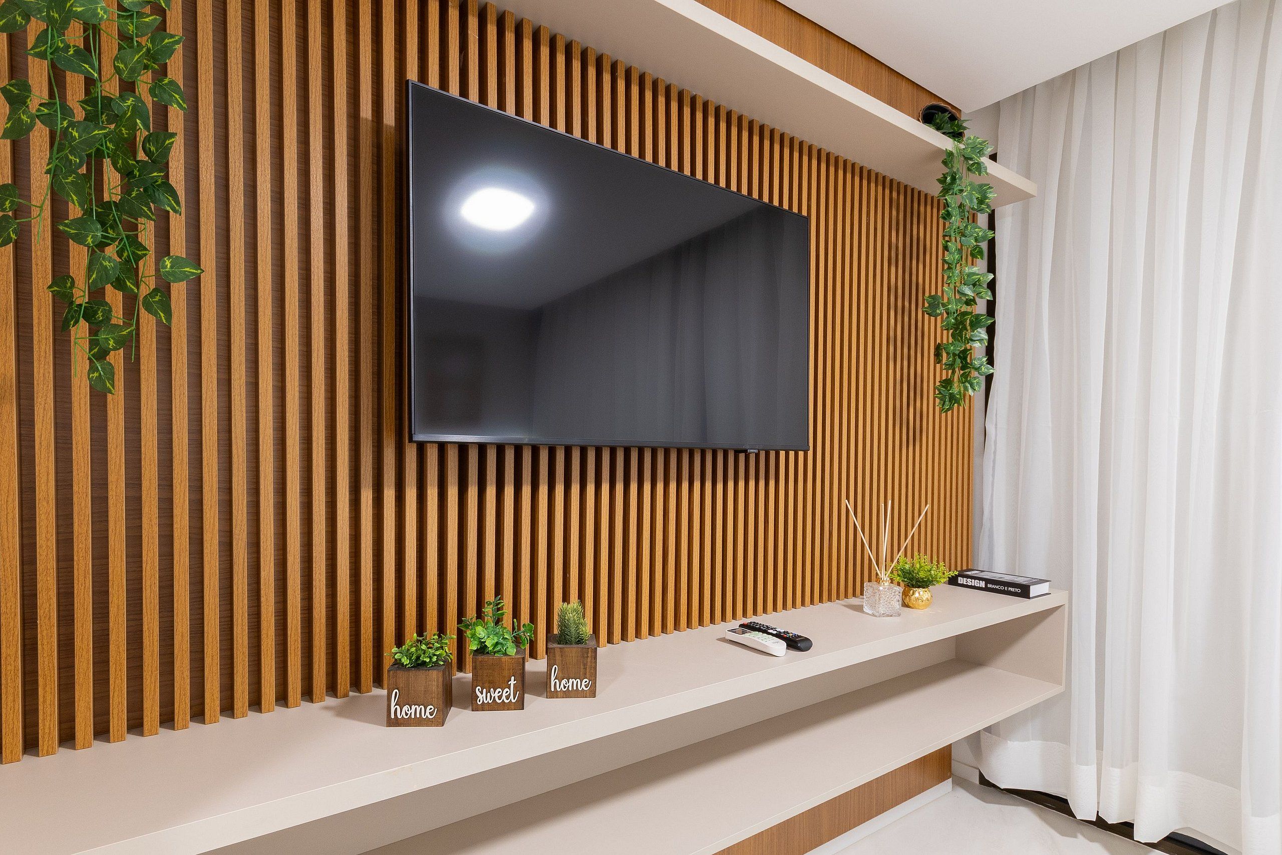 Un soggiorno moderno con una TV a schermo piatto montata su una parete di listelli di legno, uno scaffale con piante decorative e un telecomando.
