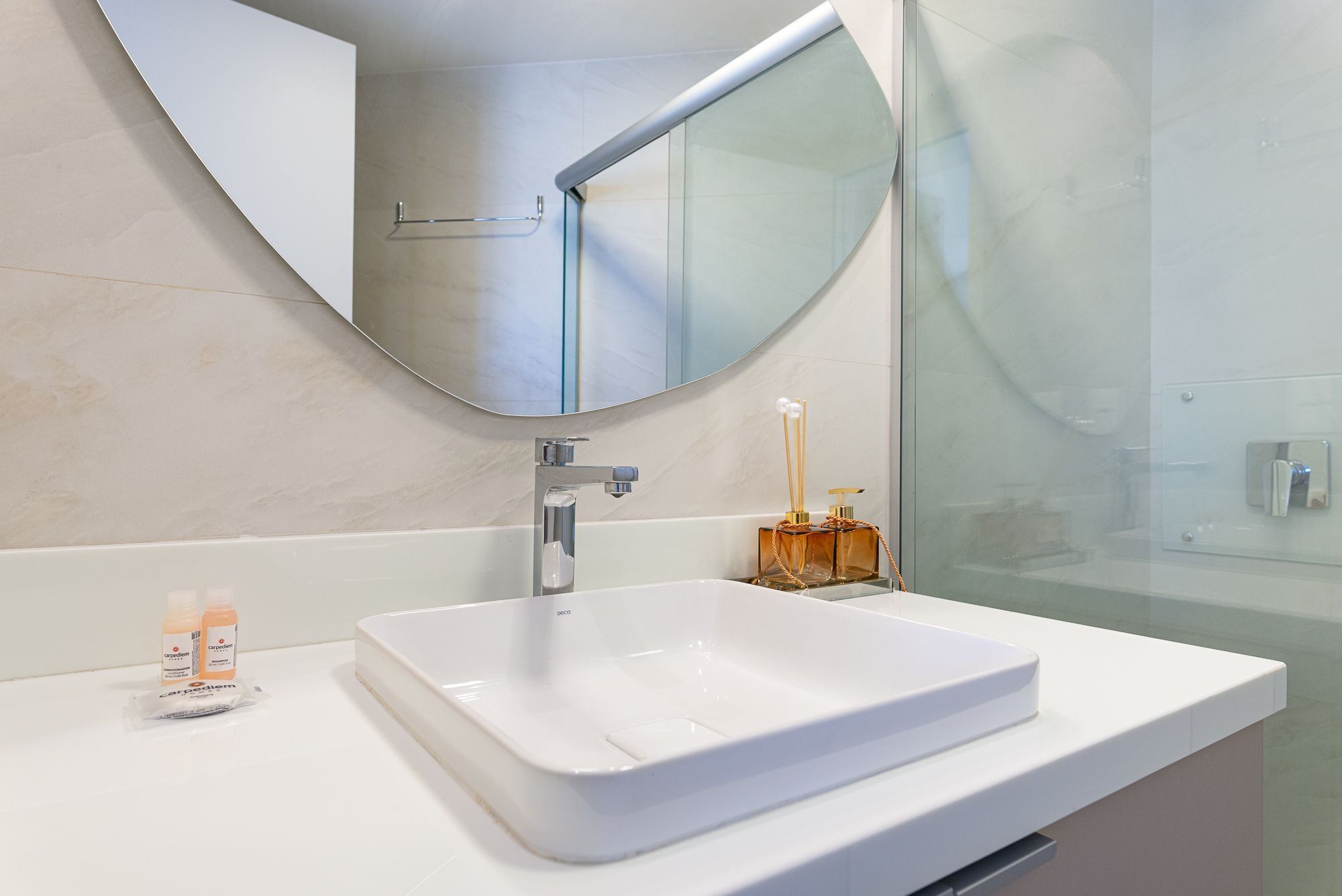 Une salle de bain moderne avec un lavabo blanc, un grand miroir et une douche à parois de verre.