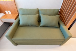 Un sofá verde con dos almohadas y una mesita de madera con un cajón blanco.