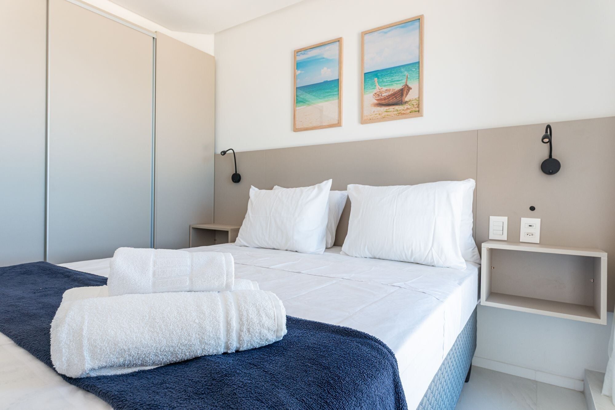 A hotel room with a bed, two wall-mounted lamps, a nightstand, and two framed pictures on the wall.