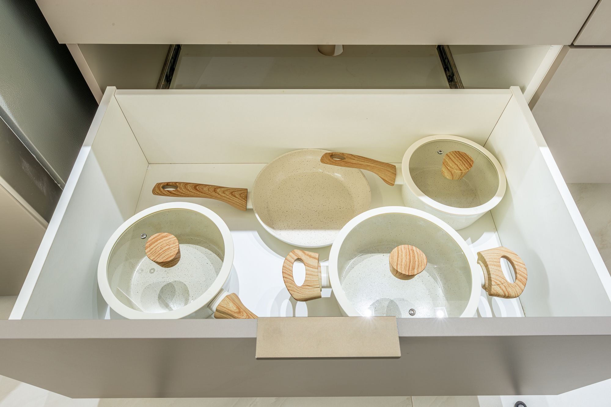 A kitchen drawer with four ceramic pots and a frying pan.
