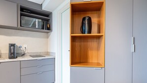 A kitchen with grey cabinets, a microwave, a kettle, and a wooden shelf unit. - Vivant New Building Seafront in Recife (Recife)