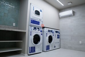 Un cuarto de lavandería con dos lavadoras de carga frontal, pared de azulejos y un equipo de aire acondicionado.