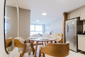 A modern kitchen with a built-in refrigerator and a dining area with a round table and wooden chairs. - Vivant New Building Seafront in Recife (Recife)