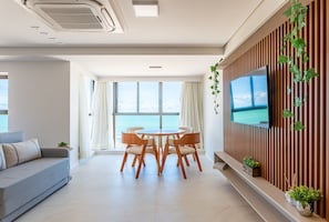 Uma sala de estar moderna com área de jantar, janelas amplas, TV de tela plana e vista para o mar.