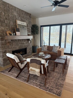 A living room with a stone fireplace, a ceiling fan, and a large window with a view of a snowy landscape. - Ski Hill Haven in beautiful Driggs, Idaho.  Sleeps up to 15 guests. (Driggs)