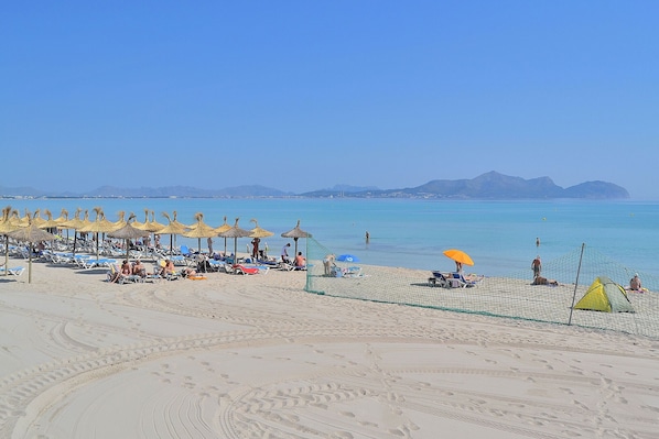 A beach with sun loungers, umbrellas, and a volleyball net.