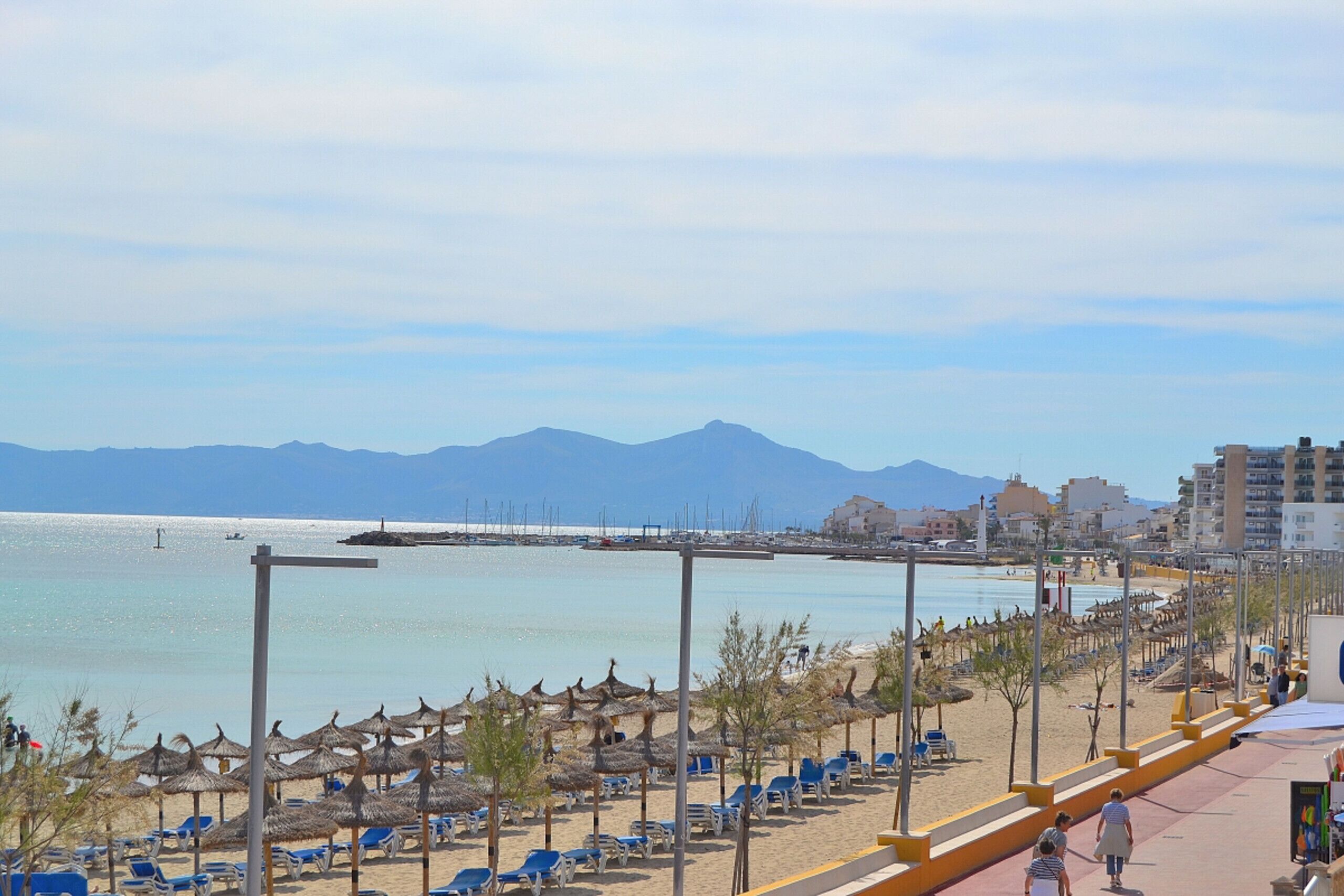A beach with umbrellas, lounge chairs, and a clear view of the sea and mountains.