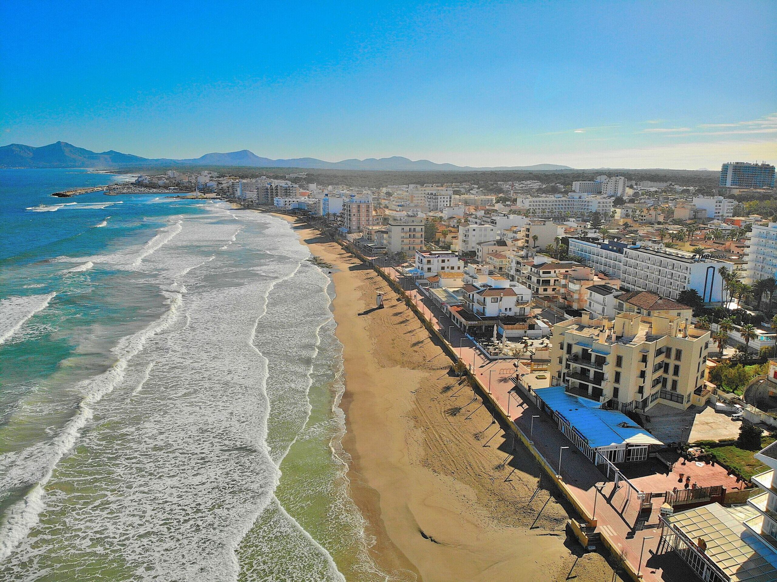 A coastal cityscape with a beach, buildings, and mountains in the background.