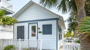 A coastal house with a white exterior, blue shutters, a wooden deck, and potted plants. - Gull Cottage (Tybee Island)