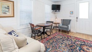 A room with a white wall, a television mounted above a table, a sofa, and a patterned rug. - Gull Cottage (Tybee Island)