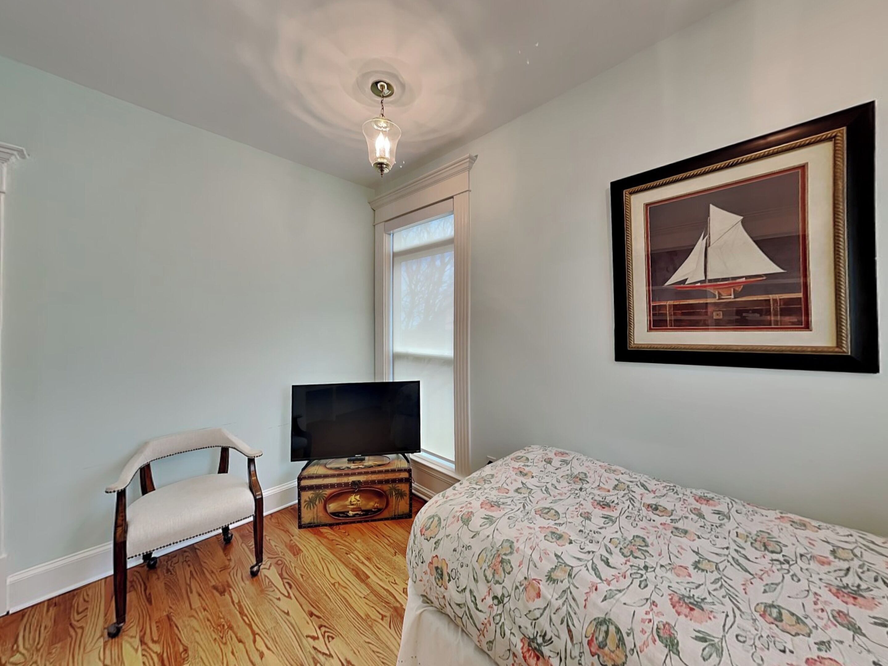 A bedroom with a bed, a TV, a chair, a wooden chest, and a framed picture on the wall.