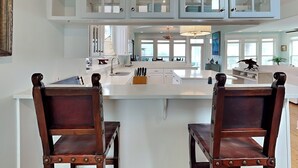A modern kitchen with white cabinetry, a central island, and two wooden chairs. - The Northshore (Tybee Island)
