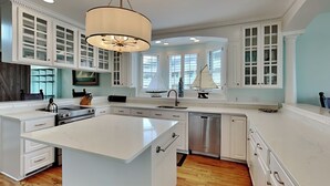 A spacious kitchen with white cabinetry, a large island, and a pendant light. - The Northshore (Tybee Island)