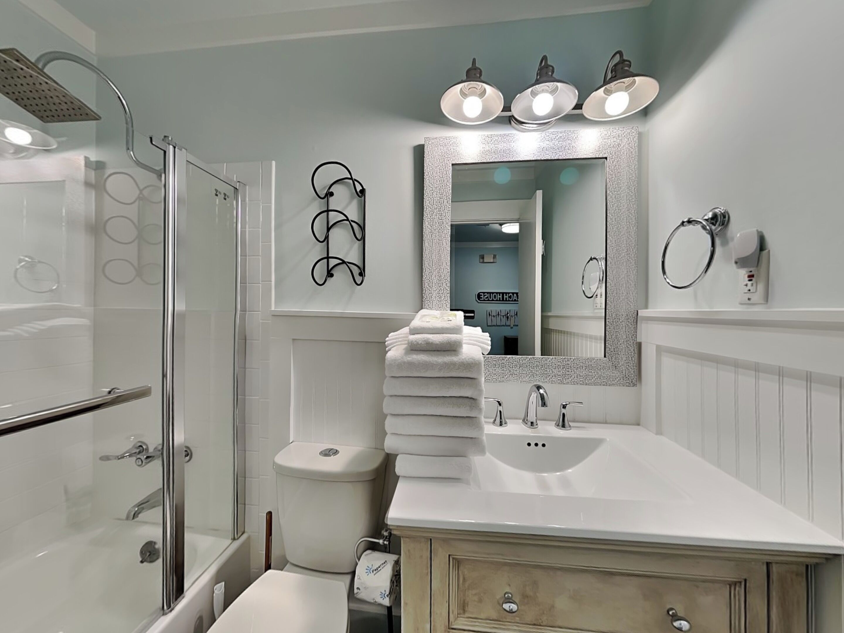 A modern bathroom with a glass shower enclosure, a white sink with a mirror above it, and a stack of white towels.