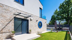 A modern building with a stone facade, a circular blue window, and a well-maintained lawn. - Luxury Villa Amarea: Private pool, summer kitchen & Istrian tranquility (Blaškovići)