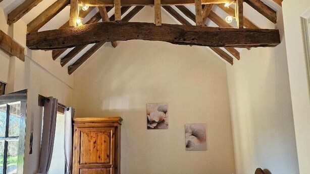 A bedroom with a sloped ceiling, wooden beams, a bed with pillows, a dresser, and a radiator. - Dickleburgh Crown (Diss)