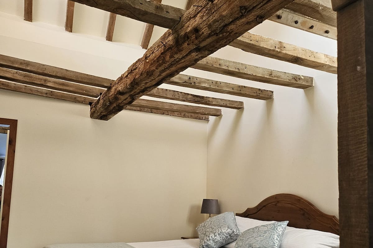 Una camera da letto con soffitto in legno, un letto con biancheria bianca e un comodino con una lampada.